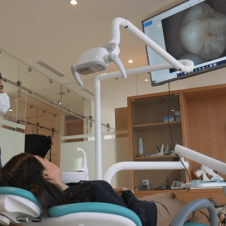 Paciente en silla dental recibiendo diagnóstico digital con monitor mostrando imagen de su boca en clínica dental moderna.